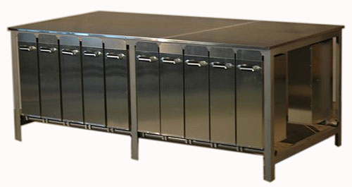 A photograph of a very large steel table, with one row of ten tall swing-out drawers facing the viewer, and another row of drawers partially hidden from view